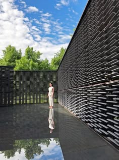 a man standing in front of a black wall next to a water fountain and trees