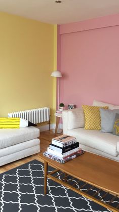 a living room with yellow and pink walls, white couches and black and white rug