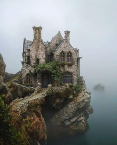 an old stone house sitting on top of a cliff next to the ocean in fog