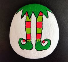 a painted rock with two green and red christmas stockings hanging from it's palm trees