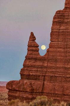 the full moon is setting behind some red rock formations in the middle of desert land