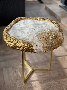 a gold and white table with some glass beads on it's legs, sitting on a wood floor