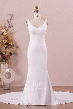 a white wedding dress on a mannequin in front of a vase with flowers