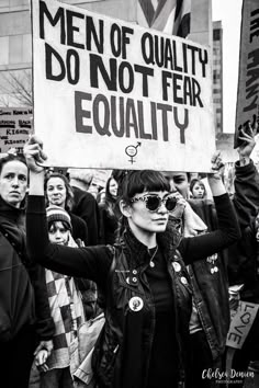 a woman holding a sign that says men of quality do not fear equality in front of other people