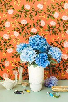 blue flowers are in a white vase on a table next to a wallpapered background