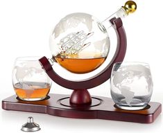 a glass globe with a ship in it and two glasses on a wooden stand next to each other