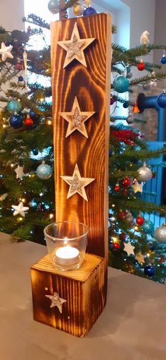 a wooden block with three stars on it and a lit candle in front of a christmas tree