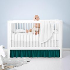 a baby laying in a white crib next to a teddy bear and blanket on the floor