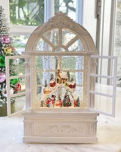 a small white window with christmas decorations on the windowsill and trees in the background