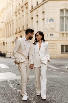 a man and woman are walking down the street holding hands while looking at each other