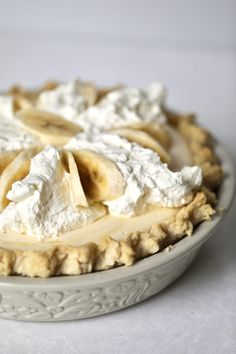 a pie with bananas and whipped cream on top sits in a white bowl, ready to be eaten