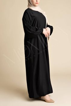 Embody the essence of modesty with our Classic Luxe Relaxed Abaya - Arwaa. A timeless black abaya that falls beautifully, creating a relaxed, a-line fit that ensures a graceful appearance. Made from the finest nida fabric, Arwaa offers a relaxed, flowy silhouette that drapes effortlessly, creating a look of sophisticated ease. This abaya blends simplicity with functionality, offering side pockets for your belongings, elastic cuff sleeves for ease during wudhu, and a back zip closure for a perfec Abaya Noir, Hijab Colors, Black Abaya, Jersey Hijab, Bamboo Shades, Relaxed Style, Cuff Sleeves, Autumn Summer, Silk Satin