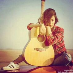 a woman sitting on the ground holding an acoustic guitar