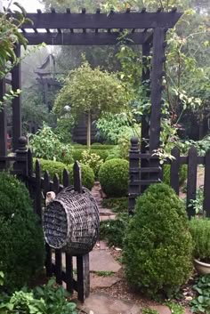 a bird cage sitting on top of a stone walkway next to a wooden arbor in a garden