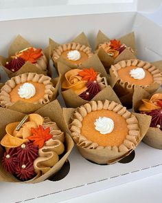 there are many small cupcakes in the box on the table with leaves and flowers