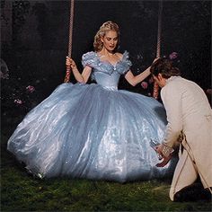 a woman in a blue ball gown on a swing with a man kneeling down next to her