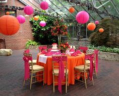 an outdoor dining area with orange and pink decorations on the table, lanterns in the background