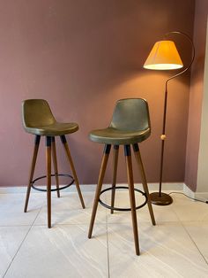 two stools sitting next to each other in front of a wall with a lamp on it