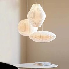 three white paper lanterns hanging from the ceiling above a round table with books on it