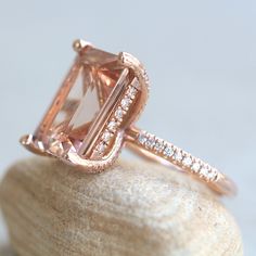 This Diamond Prong Morganite Ring is part of our Olivia Collection, which is characterized by a gorgeous, genuine gemstone with Golden Hearts under it. Diamonds stud the hidden halo and sparkle down the half eternity shank.  Custom initials at the back of the shank are available on all rings upon request!

Center Stone: Genuine AAA Peachy Pink Morganite, Emerald Cut, averaging 15x12mm and 10 carats.
Side Stones: 68 Diamonds – you choose Lab Grown or Organic – averaging F-G, VS2-SI1 and 0.46 cara Luxury Morganite Ring With Prong Setting, Elegant Radiant Cut Morganite Rings, Elegant Morganite Radiant Cut Rings, Morganite Radiant Cut Jewelry For Anniversary, Elegant Radiant Cut Morganite Jewelry, Radiant Cut Morganite Wedding Jewelry, Radiant Cut Morganite Rings For Anniversary, Morganite Diamond Ring With Accent Stones, Wedding Rings With Radiant Cut Gemstone