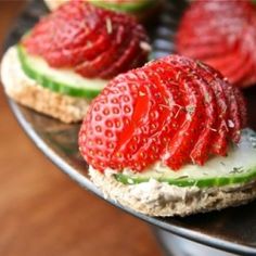 several small sandwiches with strawberries on them sitting on a metal tray next to silverware