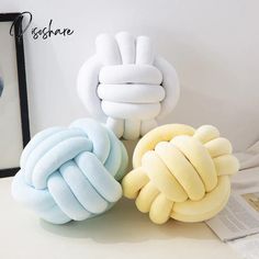 three different colored pillows sitting next to each other on a white table with a black frame