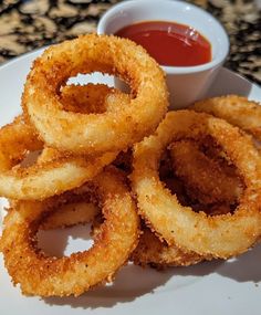 fried onion rings on a plate with ketchup and dipping sauce in the background