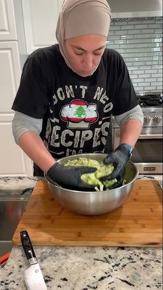 a woman in a black shirt and head scarf is making food on a wooden cutting board