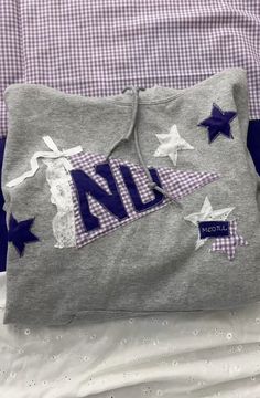 a grey sweatshirt with blue and white stars is laying on top of a purple checkered bed spread