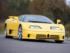 a yellow sports car is parked on the side of the road with trees in the background