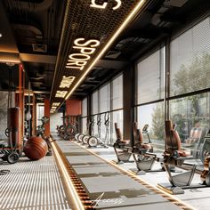 there are many exercise machines in this gym area with lights on the ceiling and large windows