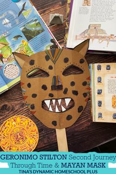 a paper mask sitting on top of a wooden table next to books and an open book