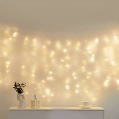 a white table topped with a vase filled with flowers next to a wall covered in lights