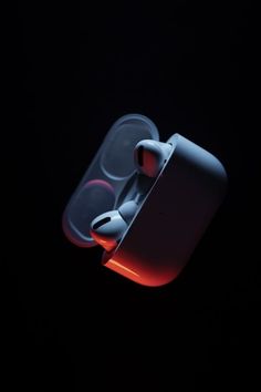 an apple airpods in the dark with red light coming from it's side