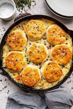 a casserole dish filled with baked biscuits and parmesan cheese, garnished with herbs