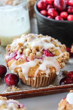 cranberry muffins with icing on a baking sheet next to fresh cranberries