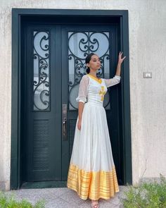 This stunning dress is a true masterpiece of Ethiopian textile art. The lower part of the dress is made from tibeb, a handwoven fabric that is known for its unique patterns and vibrant colors. The intricate design of the tibeb fabric adds a touch of elegance and cultural significance to the dress, making it perfect for special occasions. The neckline of the dress is particularly striking, featuring a cross design that is both traditional and modern at the same time. The cross represents the Ethi White Anarkali Dress In Cotton Silk, Fitted White Cotton Silk Kurta, White Fitted Cotton Silk Kurta, White Cotton Silk Dress With Traditional Drape, White Fitted Cotton Silk Traditional Wear, Embroidered Cotton Silk Floor-length Dress, Elegant White Cotton Silk Dress, Maxi Length Gown With Pallu For Traditional Ceremonies, Traditional A-line Embroidered Dress