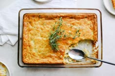 a casserole dish with a spoon in it on a table next to plates and utensils