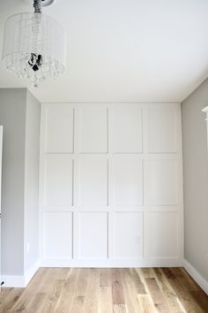 an empty room with white paneling and a chandelier