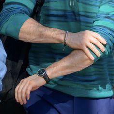 a man with his hand on the wrist of another person wearing a watch and blue pants