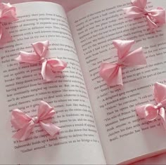 three pink bows are on top of an open book, with the pages folded down