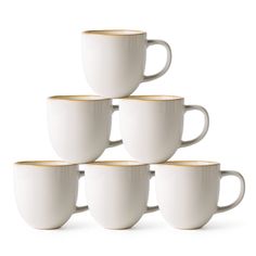 six white coffee cups with gold rims stacked in a pyramid on a white background