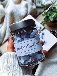 a person holding a jar filled with blue and white confetti next to a potted plant