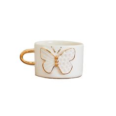 a white and gold cup with a butterfly on the side, sitting on a white surface