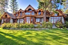 a large wooden house sitting in the middle of a lush green field with lots of trees