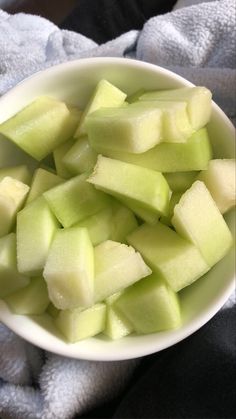 a white bowl filled with sliced apples on top of a table next to a gray towel