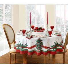 a dining room table set for christmas with red candles and holly wreaths on it