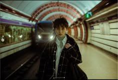 a young man standing in front of a train at a subway station with his hand on his hip