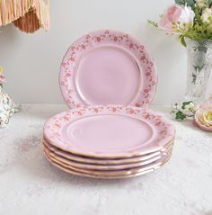 pink plates stacked on top of each other with flowers in vases behind the plates