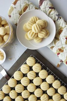 some cookies are on a cooling rack next to a bowl of sugar and two bowls of nuts